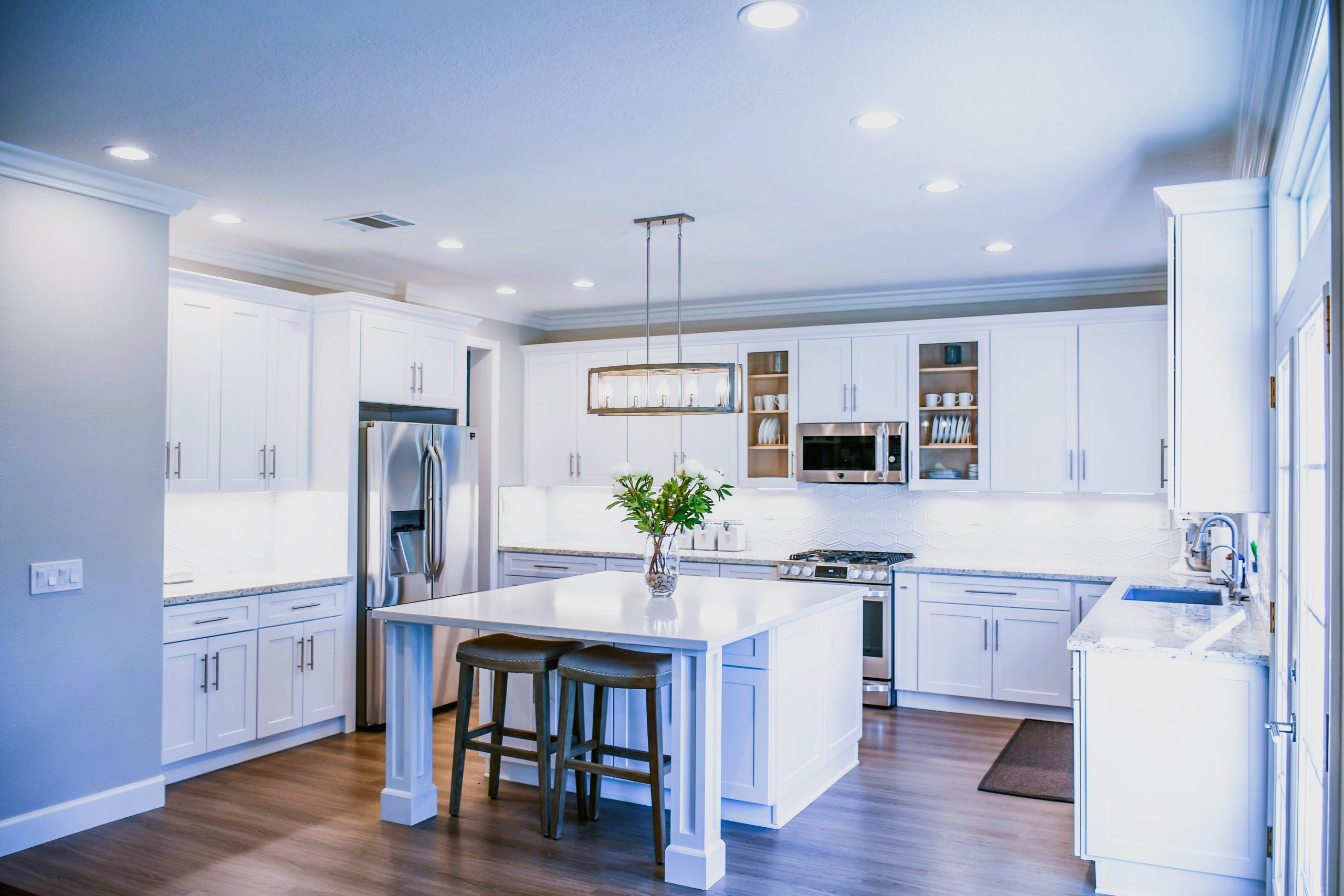 Bright and modern white kitchen with island and stainless steel appliances, professionally cleaned.
